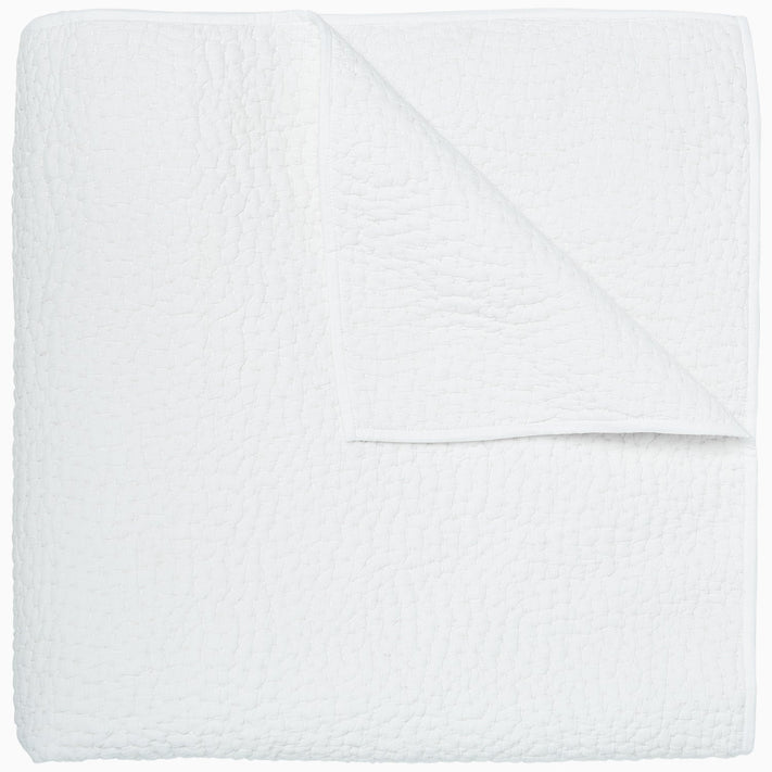 An Organic Hand Stitched White Quilt by John Robshaw folded on top of a white surface.