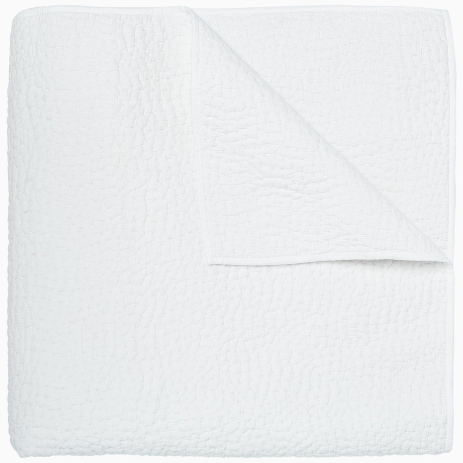 An Organic Hand Stitched White Quilt by John Robshaw folded on top of a white surface.