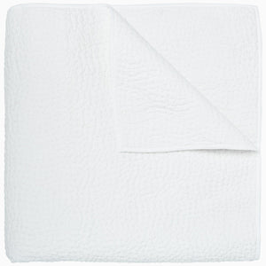 An Organic Hand Stitched White Quilt by John Robshaw folded on top of a white surface.