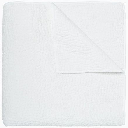 An Organic Hand Stitched White Quilt by John Robshaw folded on top of a white surface.