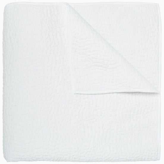 An Organic Hand Stitched White Quilt by John Robshaw folded on top of a white surface.