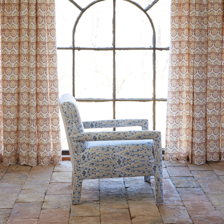 The John Robshaw Square Chair in Marmar Marigold and Natesh Sand, featuring custom upholstery and performance fabric, is shown facing left on a tiled floor in front of a large arched window with patterned curtains.