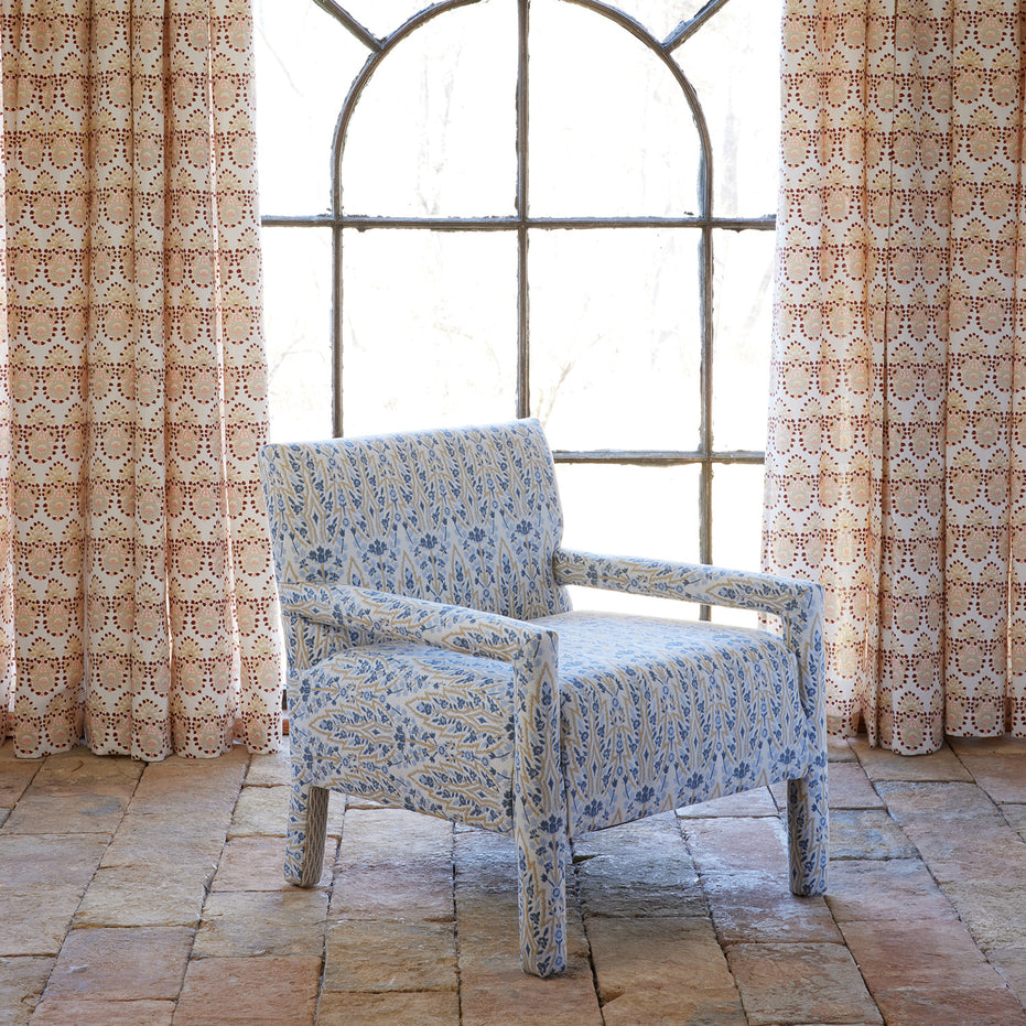 The Square Chair in Marmar Marigold and Natesh Sand by John Robshaw, upholstered in a vibrant performance fabric, sits on a tiled floor in front of a tall arched window with patterned curtains.