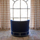 A John Robshaw Round Swivel Chair in Bijal Indigo Performance Fabric, featuring nailhead trim and a swivel base, faces a large arched window, flanked by patterned curtains on a stone tile floor.