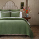 A neatly made bed with Anketi Sage Organic Sheet Set by John Robshaw, white pillows, a geometric headboard, and a wooden side table with flowers in a softly lit bedroom.