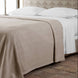 A bed with the Anketi White Organic Sheet Set by John Robshaw, white pillows, and a beige blanket sits on rustic tiles with a patterned headboard in the background.