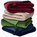 A stack of John Robshaw Velvet Moss Throws with tassels, crafted by Indian artisans. - 30497693892654