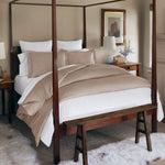 A neatly made four-poster bed adorned with the Huma Sand Duvet Set from John Robshaw, flanked by wooden nightstands, a bench at the foot, and a rug underneath in a well-lit bedroom. - 31249529897006