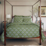 A bedroom with a hand quilted four-poster bed featuring the John Robshaw Jeeva Sage Quilt, a white lamp on a nightstand, a framed picture on the wall, and a branch in a vase on the opposite nightstand. - 31258911080494