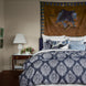 A hand-painted wall hanging complements the Indigo Elephant Decorative Pillow by John Robshaw on a bed, adorned with cotton linen.