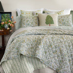 A John Robshaw bed with the Tiya Periwinkle Woven Quilt, featuring a soft periwinkle and white floral pattern. - 30395682684974
