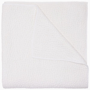 The Organic Hand Stitched White Quilt by John Robshaw features a beautifully textured, white woven design with one corner turned up to reveal its intricate hand stitching on both sides—ideal for layering with organic cotton quilts or other hand-stitched bedding to bring warmth and refined elegance to any bedroom.