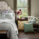 A hand block printed Verdin Dark Sage Decorative Pillow by John Robshaw on a bed in a room with a window.
