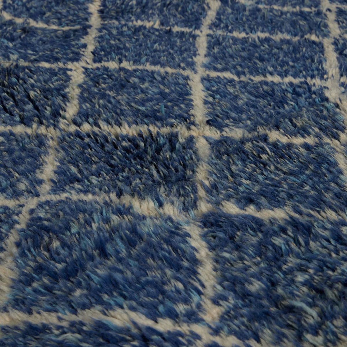 Shaggy blue John Robshaw Blue Village Wool Rug with a white grid pattern.