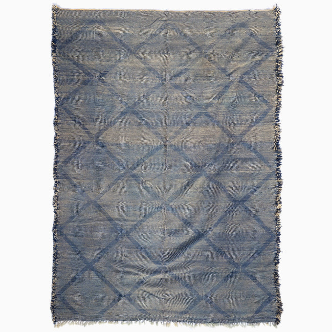 John Robshaw Big Zanafi Wool Rug, a handwoven rectangular rug featuring a blue and white diamond pattern and fringed edges, inspired by traditional Berber designs.