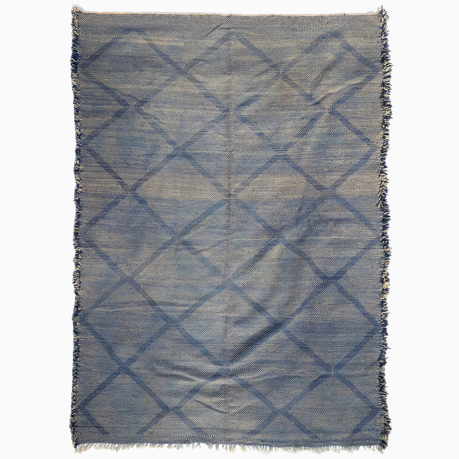 John Robshaw Big Zanafi Wool Rug, a handwoven rectangular rug featuring a blue and white diamond pattern and fringed edges, inspired by traditional Berber designs.