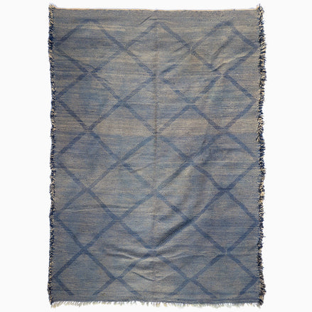 John Robshaw Big Zanafi Wool Rug, a handwoven rectangular rug featuring a blue and white diamond pattern and fringed edges, inspired by traditional Berber designs.