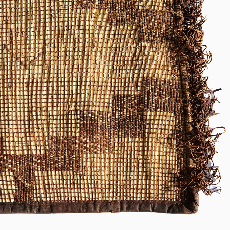 John Robshaw Tazarine Tuareg Mat with a brown geometric pattern, dark leather border, and fringed edge.