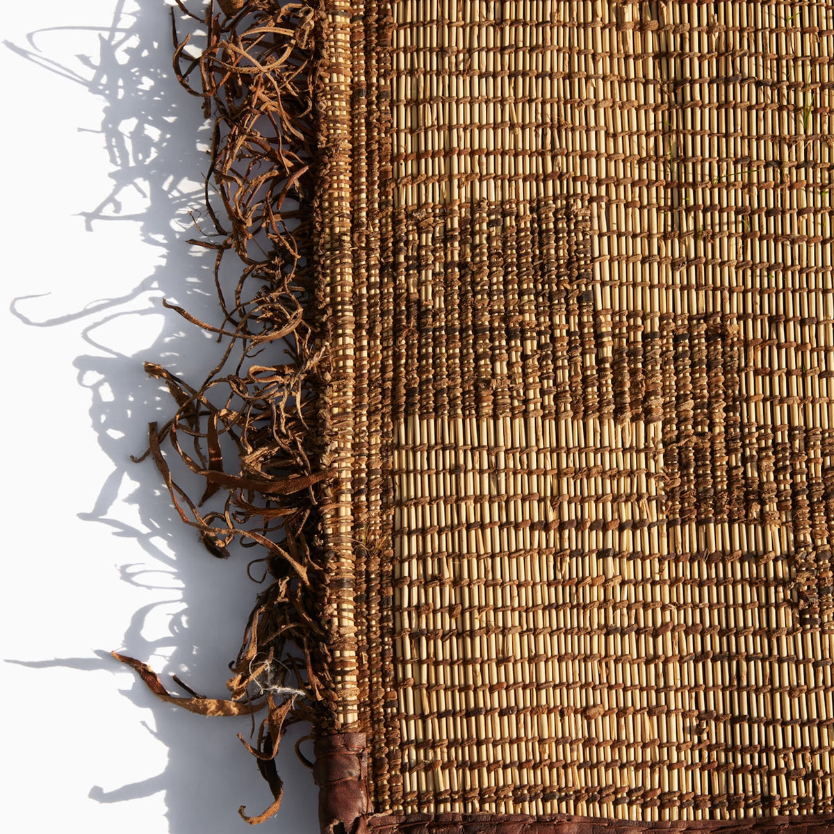 Close-up of a handwoven Tazarine Tuareg Mat with a dark brown leather border and a frayed, stringy edge.