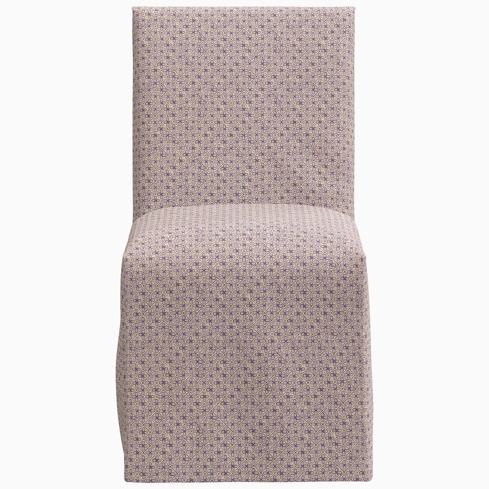The John Robshaw Sadia Slipcover Chair is a stylish dining chair with a purple patterned slipcover that beautifully contrasts against its white background.