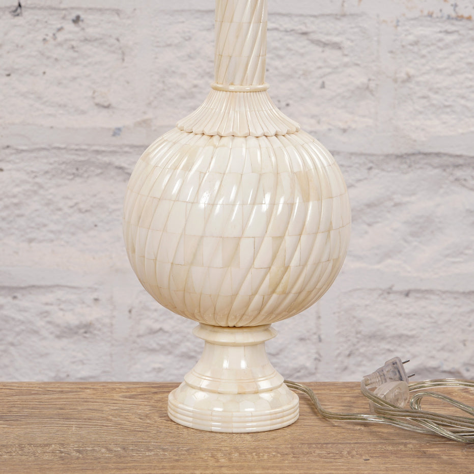 The Shiva Bone Inlay Lamp by John Robshaw sits on a wooden surface, featuring a cream-colored, textured round base and accompanied by a clear electrical cord and plug. Its handcrafted appearance is inspired by classic Mughal ginger jar designs.
