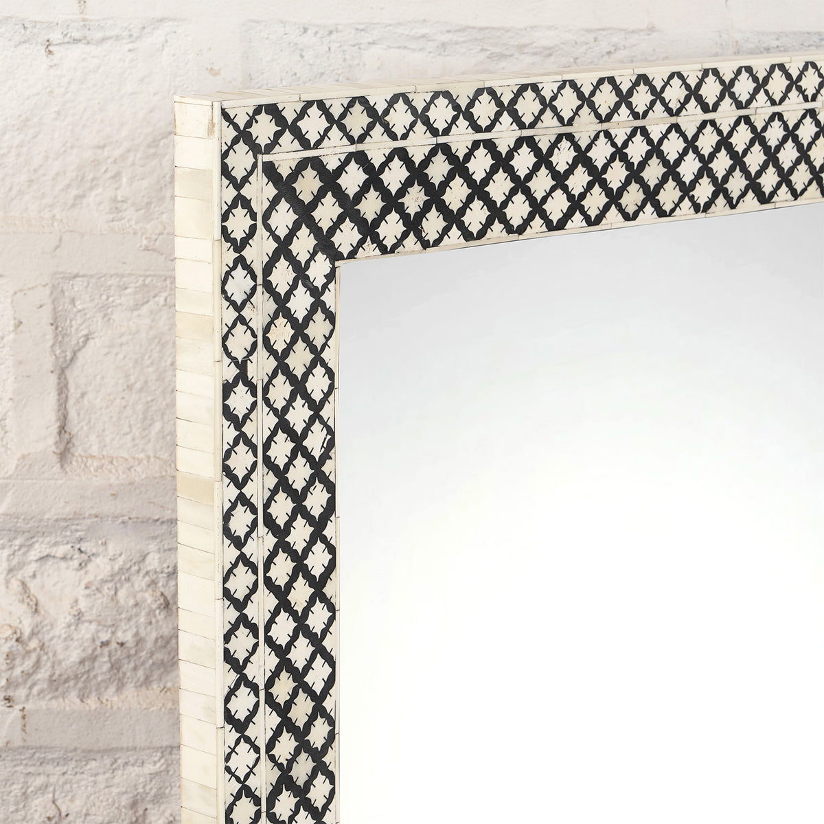 Close-up of the Arohi Bone Inlay Mirror by John Robshaw, featuring a rectangular diamond pattern with a black and white geometric frame, mounted on a white textured brick wall.