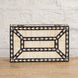 The Charita Bone Inlay Box by John Robshaw, featuring a geometric black and white striped pattern, sits on a teak wooden surface against a white brick wall.