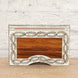 The Harini Bone Inlay Box by John Robshaw is a rectangular decorative wooden piece, handcrafted with intricate vine patterns and a light border, shown here set against a white brick wall and wooden surface.