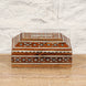 The Sita Bone Inlay Box by John Robshaw features a rectangular teak wood construction with intricate bone inlay patterns in white and brown—some delicately formed into floral motifs—beautifully displayed on a wooden surface against a white brick wall backdrop.