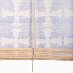 The Jaya Azure Chik Blinds by John Robshaw Textiles feature a fabric with a blue botanical pattern and a woven bamboo slat reminiscent of Indian chik blinds, complete with a central cord. - 31879863992366