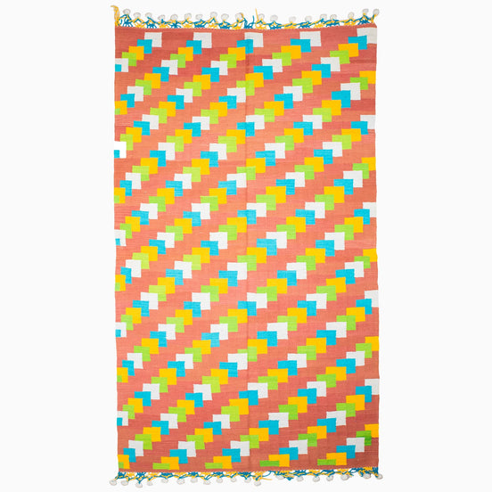 A vibrant beach towel featuring a stylish pattern of triangles, reminiscent of vintage rugs from Punjab's weaving centers, the Left to Right Then Back Again Rug by John Robshaw.