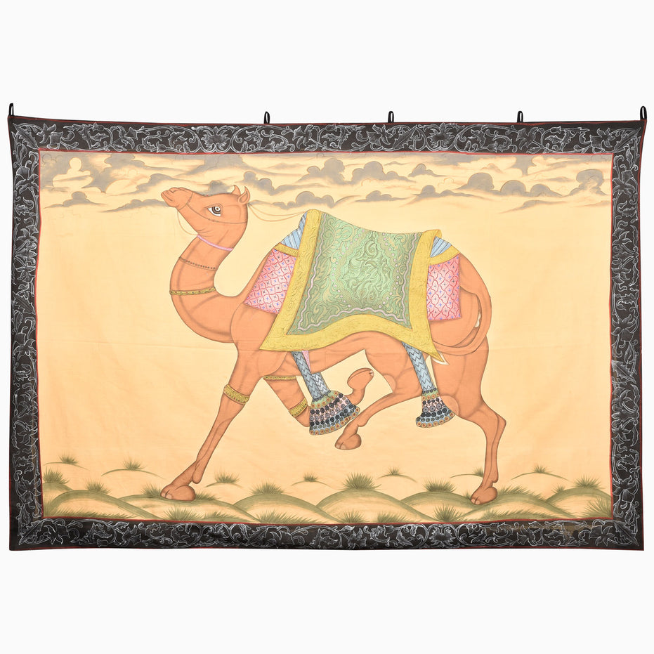 John Robshaw Cantering Camel Tapestry featuring hand-painted Rajasthan art of a camel in motion, wearing an ornate saddle and beaded anklets, framed by a dark, floral patterned border.