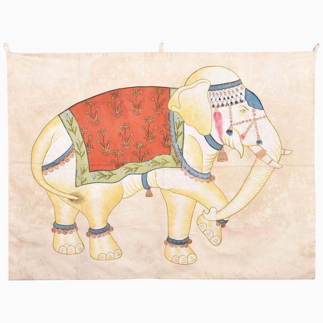 A hand-painted John Robshaw White Elephant Walking Tapestry featuring a walking elephant adorned with a floral red blanket, decorative headpiece, and ankle bells.