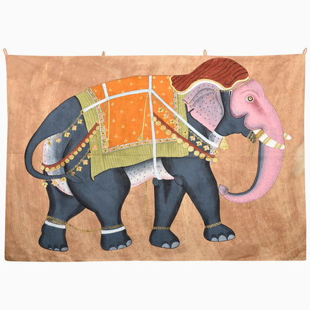 The On the Move Again Tapestry is a hand-painted piece depicting a stylized elephant with a pink head and trunk, wearing an orange and yellow embroidered jhool with gold tassels.