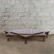 An 8 Point Wooden Bajot by John Robshaw, featuring a low, octagonal design inspired by vintage Rajasthani furniture and crafted from teak with short legs, is positioned against a white brick wall on a concrete floor.