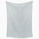 The Lavanya Mist Throw by John Robshaw, a light blue rectangular fabric with fringed edges and subtle herringbone weave, hangs against a white background.