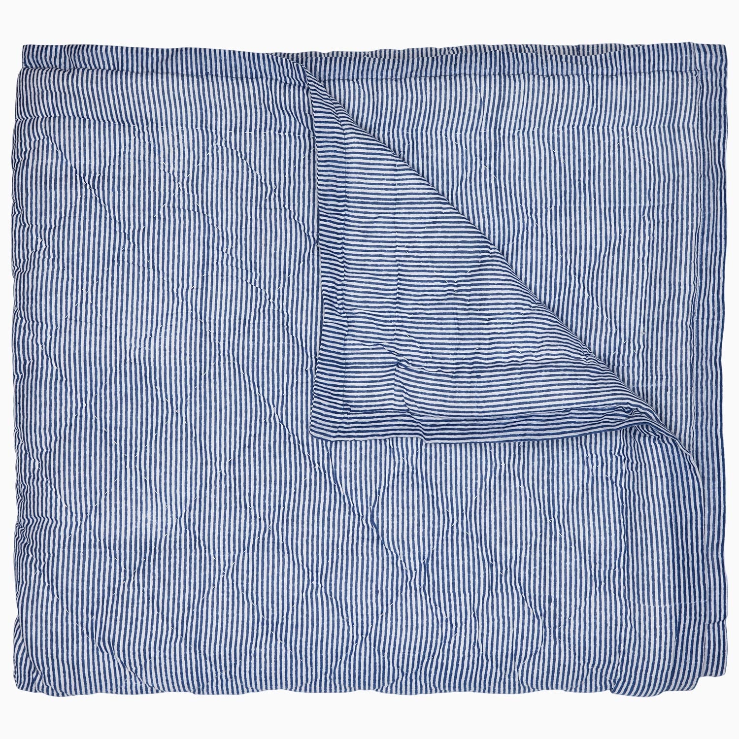 A Nandi Indigo Quilt by John Robshaw, hand quilted and featuring blue stripes, folded on top of itself.