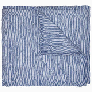 A Nandi Indigo Quilt by John Robshaw, hand quilted and featuring blue stripes, folded on top of itself.