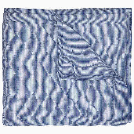 A Nandi Indigo Quilt by John Robshaw, hand quilted and featuring blue stripes, folded on top of itself.