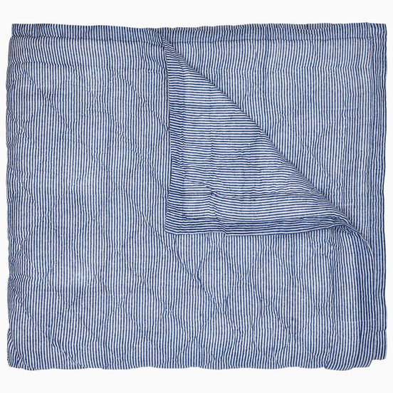 A Nandi Indigo Quilt by John Robshaw, hand quilted and featuring blue stripes, folded on top of itself.