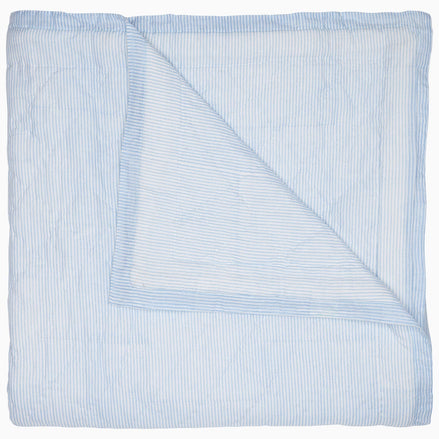 A Nandi Light Indigo quilt by John Robshaw with blue and white striped block printing on a white background.