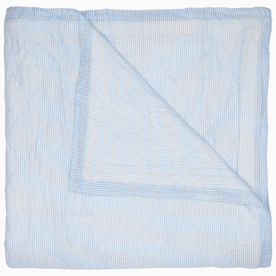A Nandi Light Indigo quilt by John Robshaw with blue and white striped block printing on a white background.