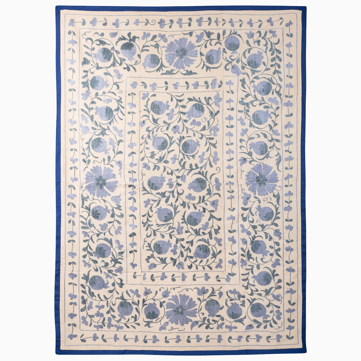 John Robshaw Azure Bloom Suzani blanket, a rectangular vintage piece with a cream background, blue floral and pomegranate embroidery, and a solid blue border.