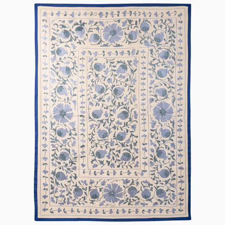 John Robshaw Azure Bloom Suzani blanket, a rectangular vintage piece with a cream background, blue floral and pomegranate embroidery, and a solid blue border.