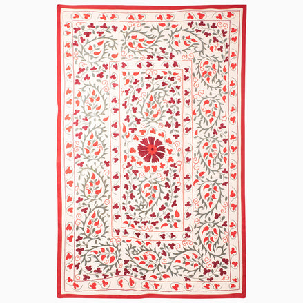 John Robshaw Come Along Then Suzani blanket in cream with a red border and an embroidered pattern of red and grey floral vines surrounding a central flower.