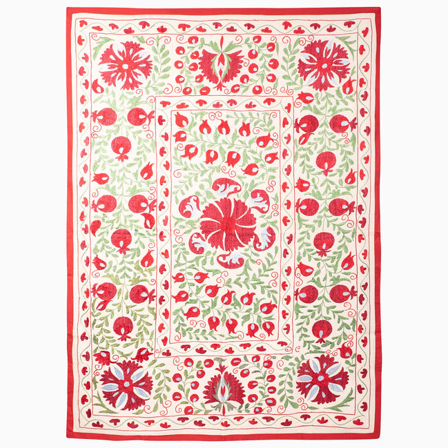 Crimson Bloom Suzani Blanket: an off-white rectangular vintage textile featuring red and green floral and pomegranate embroidery, framed by a red border.