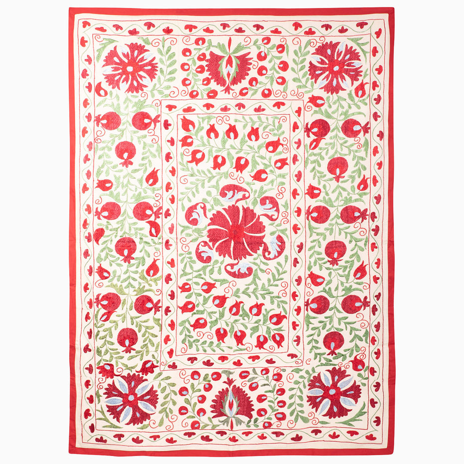 Crimson Bloom Suzani Blanket: an off-white rectangular vintage textile featuring red and green floral and pomegranate embroidery, framed by a red border.
