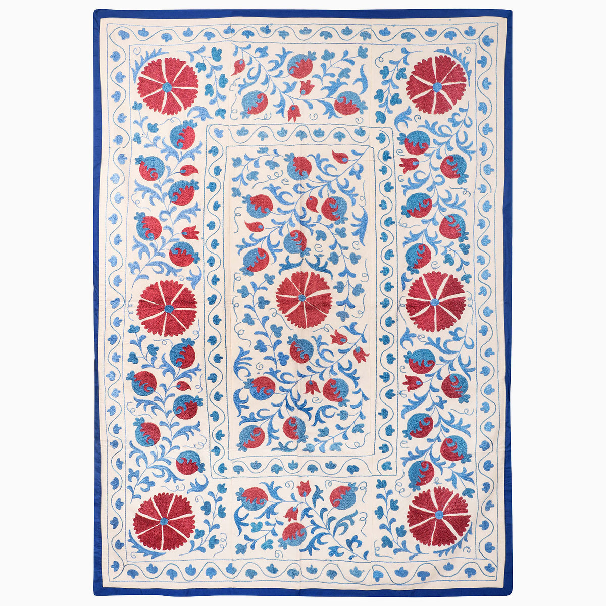 Jaipur Twilight Suzani Blanket: an off-white rectangular textile with blue and red botanical motifs in a traditional Suzani pattern and a solid blue border.