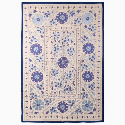 John Robshaw Open Water Suzani blanket, a rectangular vintage piece with blue floral and vine embroidery on a light background framed by a solid indigo fabric border.