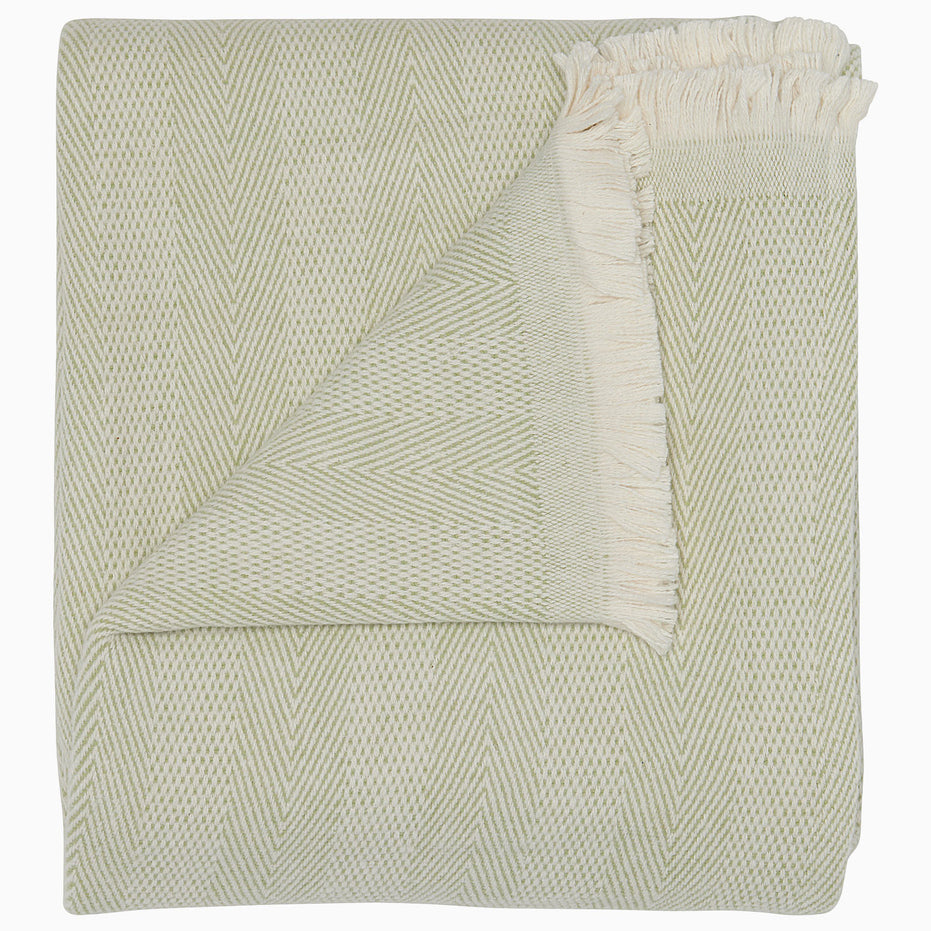 The Lavanya Sage Throw by John Robshaw is a folded, light cotton blanket featuring a subtle herringbone pattern and one fringed edge.